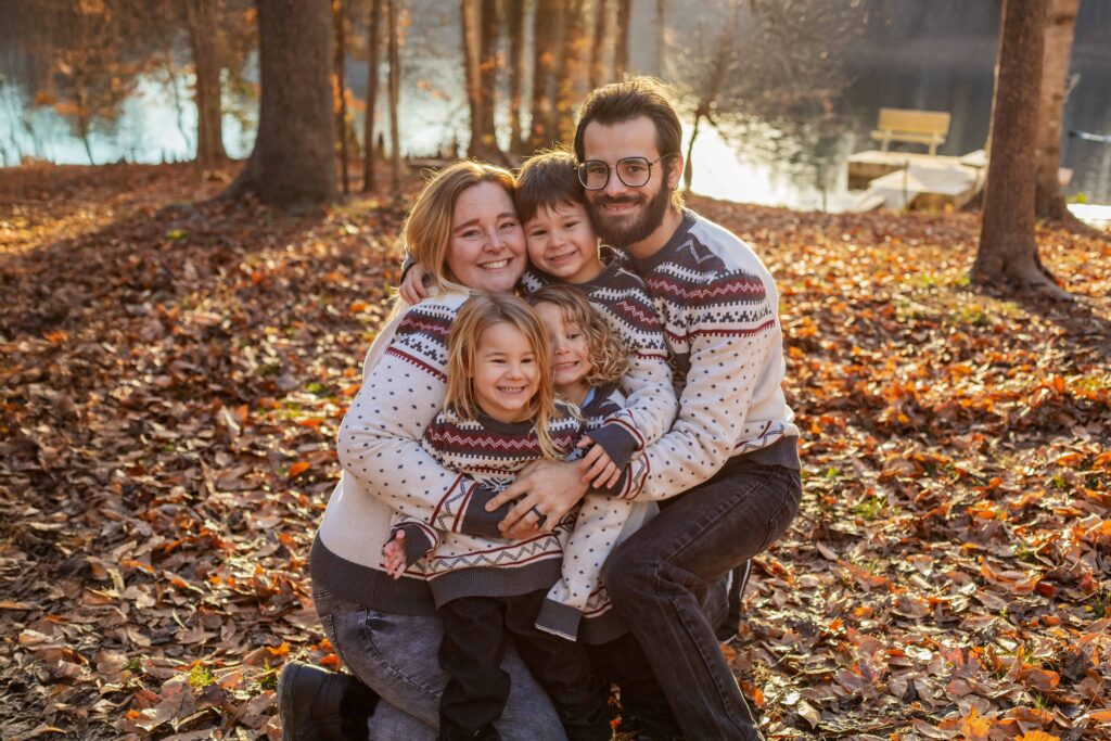 Couple and their three young children hugging lovingly, on a Private Property in Suffolk Virginia, at sunset in November with the golden hour light reflecting off the river behind them.